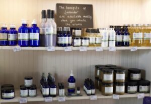 Two shelves against a white wall of tonics, soaps, and lotions in extravagant bottles. There is a sign that reads "the benefits of lavender are available mostly when you inhale the aroma."