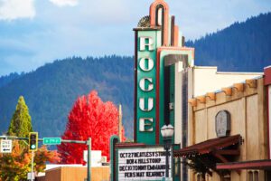 The Rogue Theater spotted at the corner of 7th street, is a vintage building with a large vertical sign reading “Rogue”. The letters are white with led lighting, the lights are off as it is a sunny day with vibrant colors.