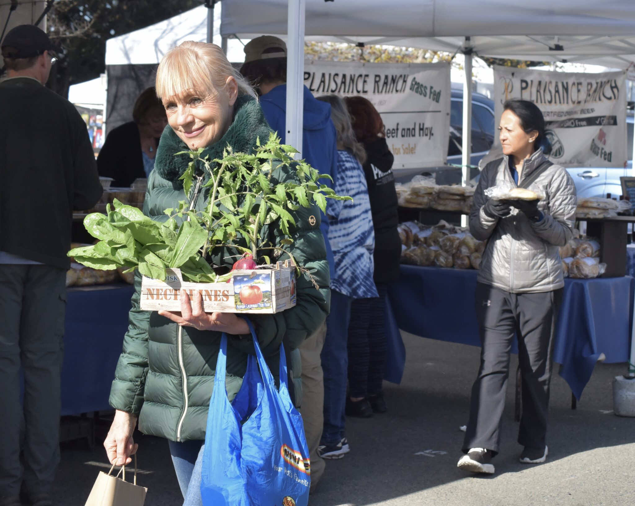 People are carrying their local produce and baked goods they purchased from the farmers market.