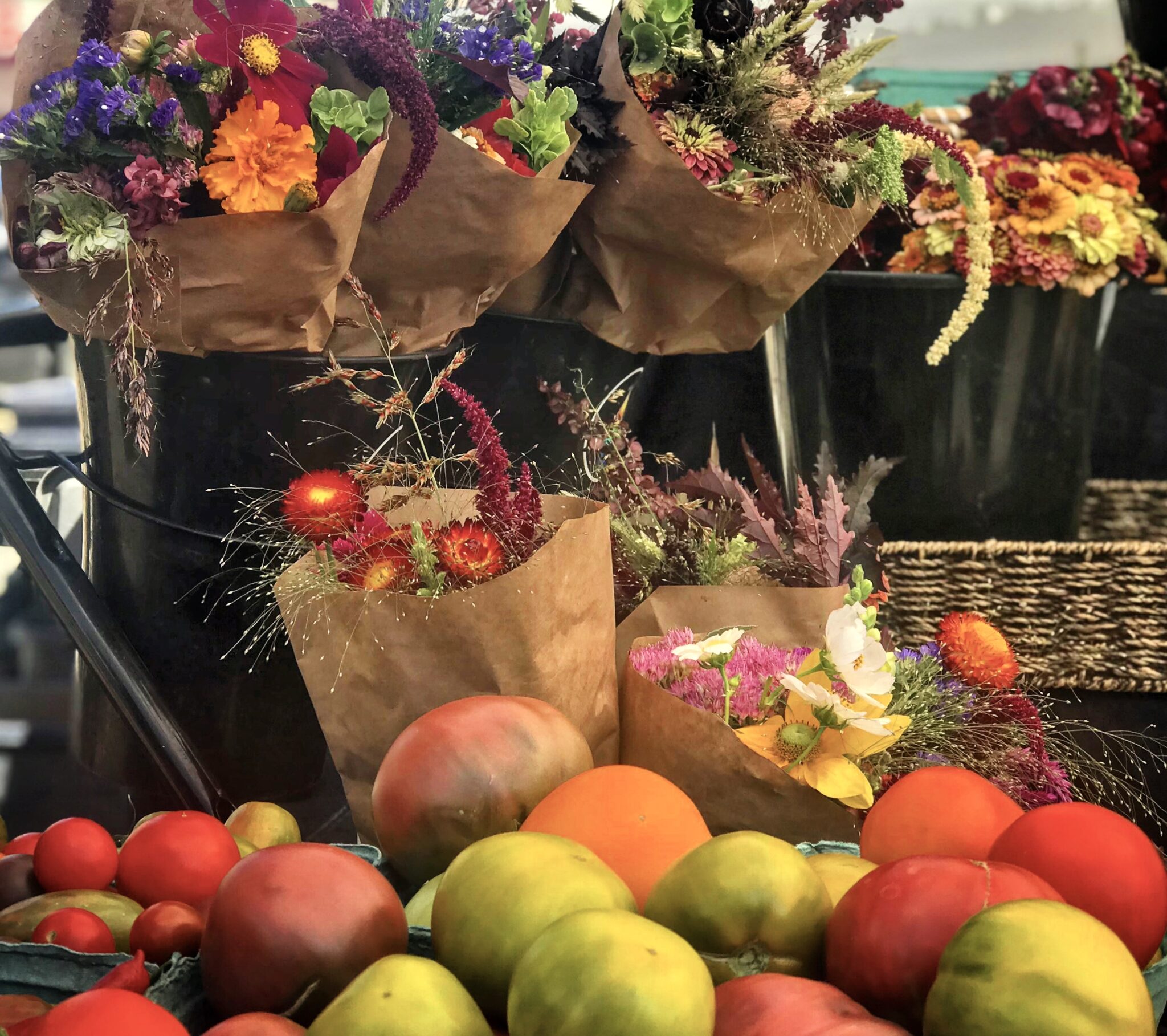 An assortment of green and red apples piled in front of multiple bouques of beautiful flowers.
