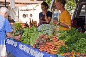 Produce stands at the grower's market. Two people are standing behind the table where produce is piled high.