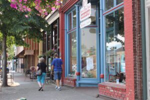 Storefronts in downtown Grants Pass with large street-facing windows framed by bricks. Boutique items of all kinds are displayed for window shopping.
