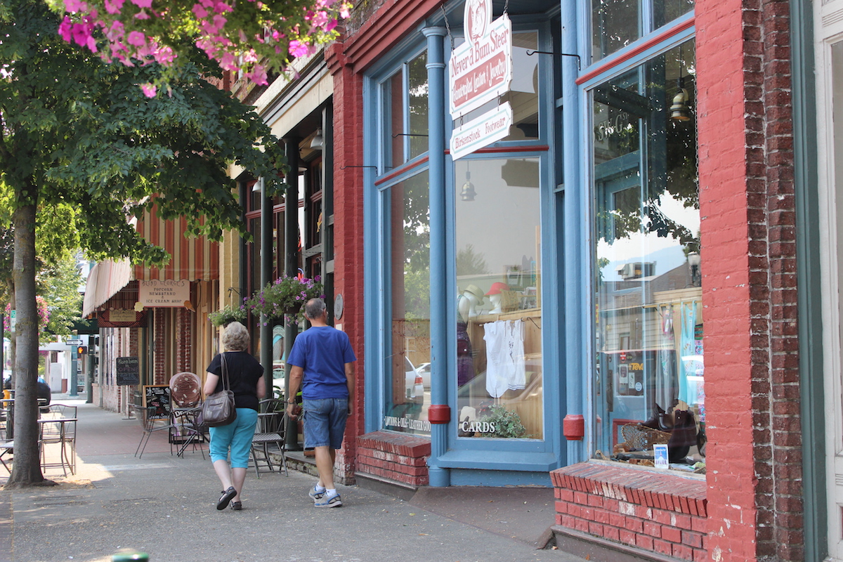 Storefronts in downtown Grants Pass with large street-facing windows framed by bricks. Boutique items of all kinds are displayed for window shopping.