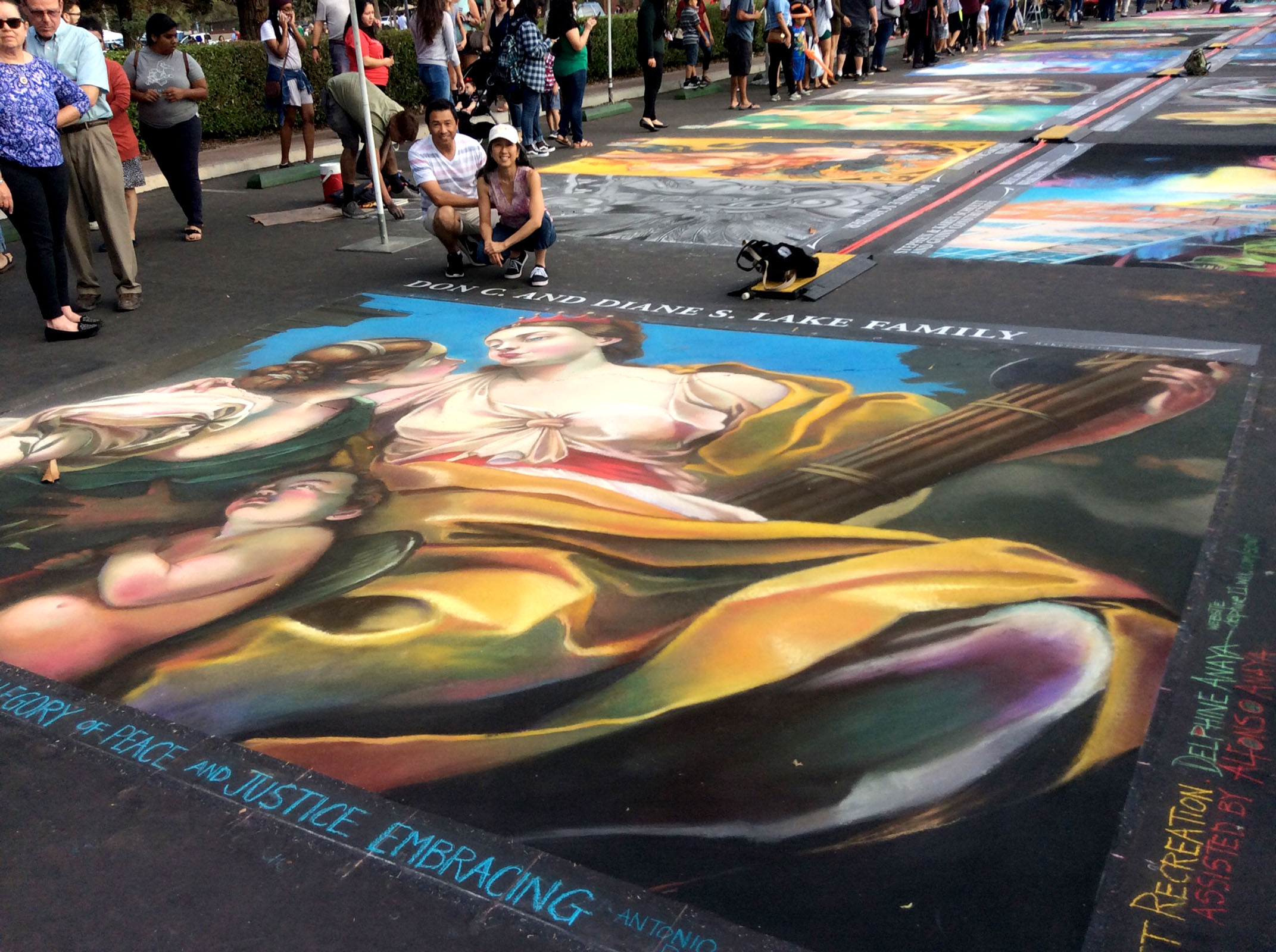 Renaissance-style chalk art on the street during a fair in downtown Grants Pass. People are crowded around the extravagant artwork.