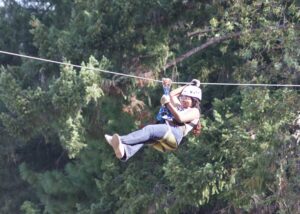A young person is ziplining through the trees at the Out N About attraction.
