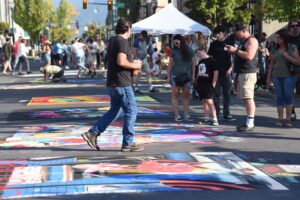 Chalk murals on the street throughout downtown Grants Pass, with pedestrians walking around viewing the artwork.