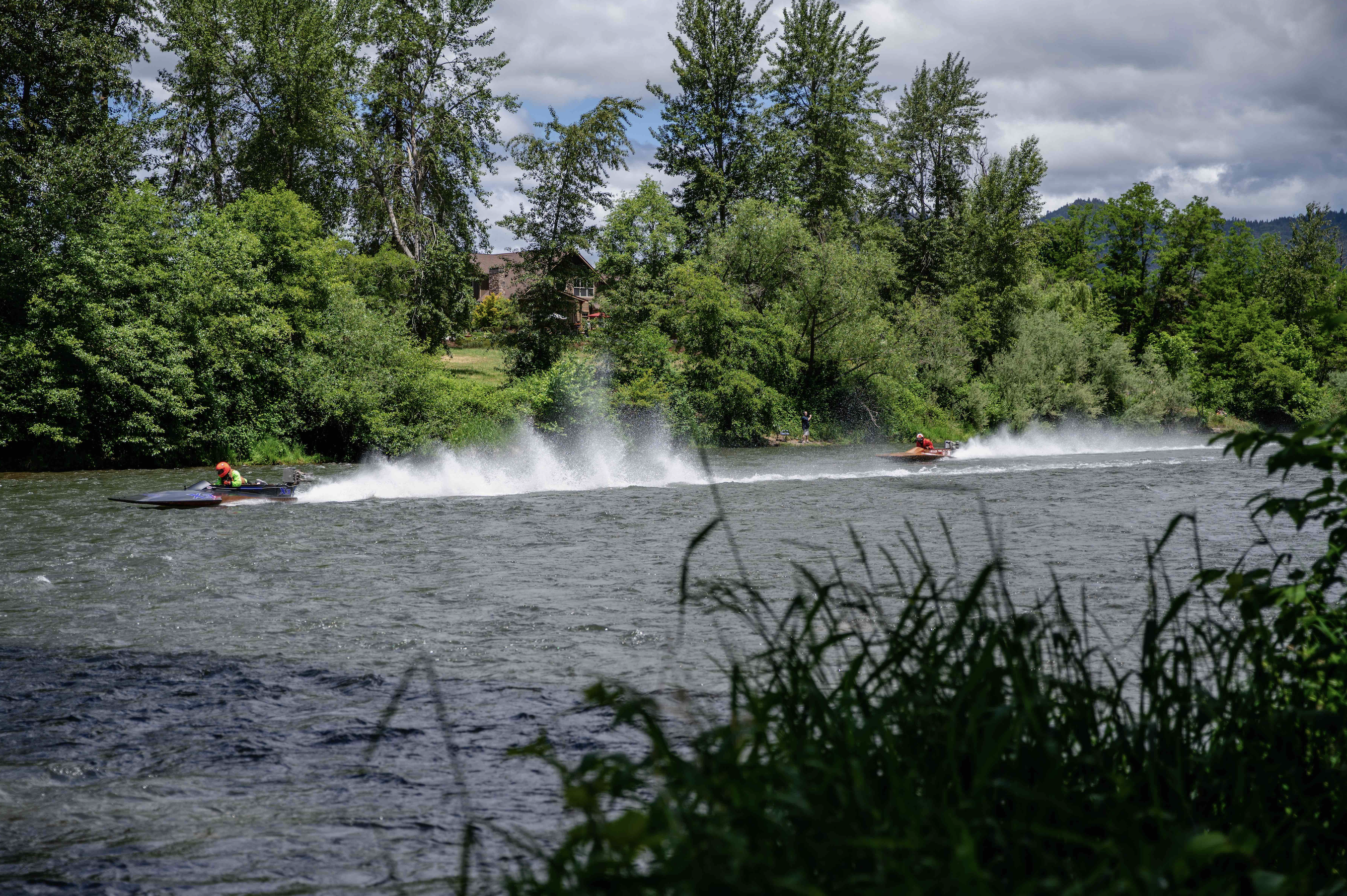 Two jet skis are cruising down the Rogue River, leaving a rift of water behind them.