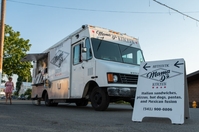 View of a white food truck with an A-frame sign in front of it, reading Mama Ds kitchen.