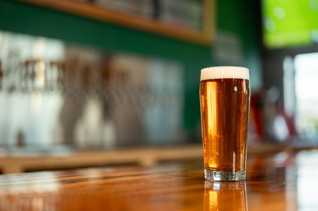 A pint of beer sits on the bar counter with the perfect amount of foam, in front of the taps that are unfocused in the background.