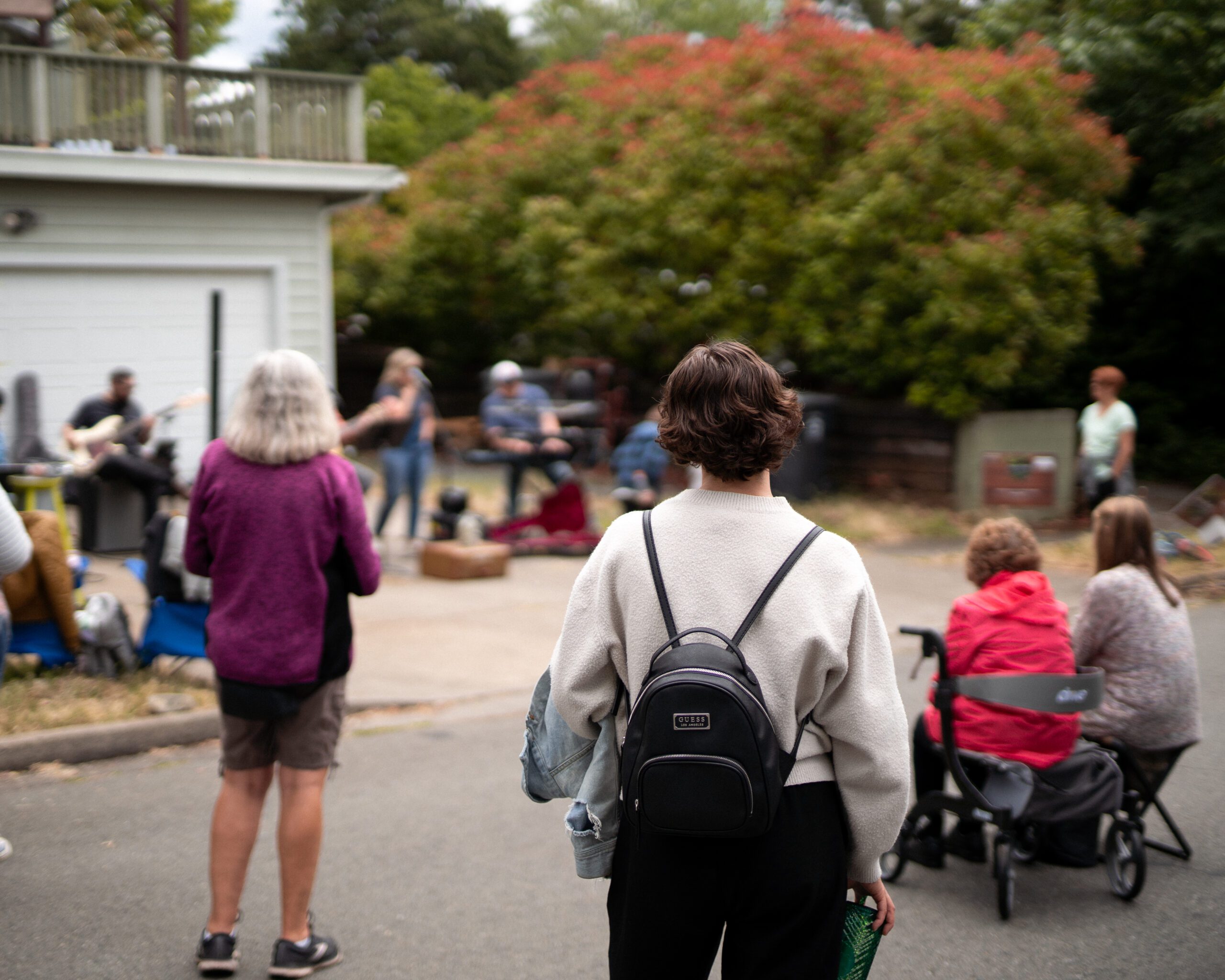 Porchfest, crowd gathers on the street in front of live music being performed on the front porch of a house.