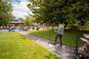 Porchfest, crowd gathers on the street in front of live music being performed on the front porch of a house.