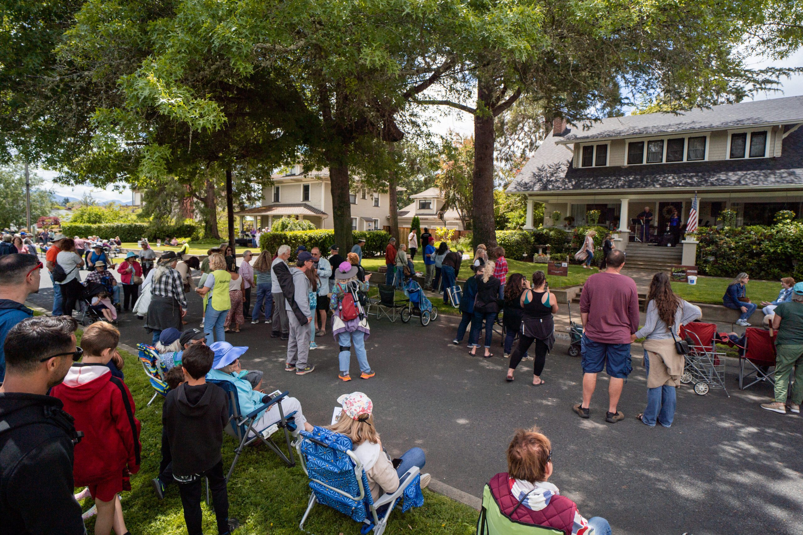 Porchfest, crowd gathers on the street in front of live music being performed on the front porch of a house.