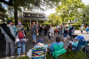 Porchfest, crowd gathers on the street in front of live music being performed on the front porch of a house.