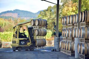 Forklift moving barrels of wine with a scenic vineyard view in the background.
